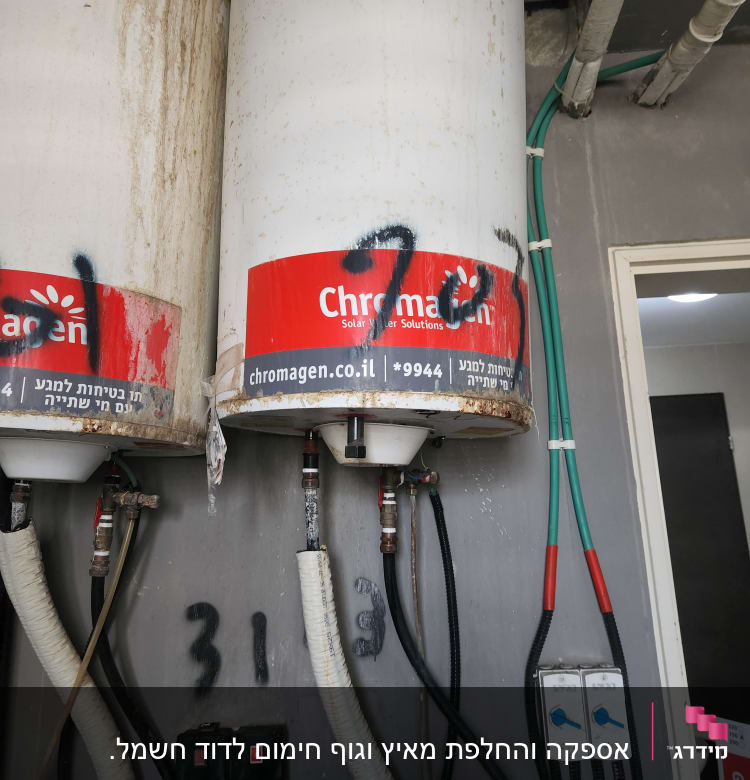 דודי שמש עם צינורות וחיבורים על קיר אפור
